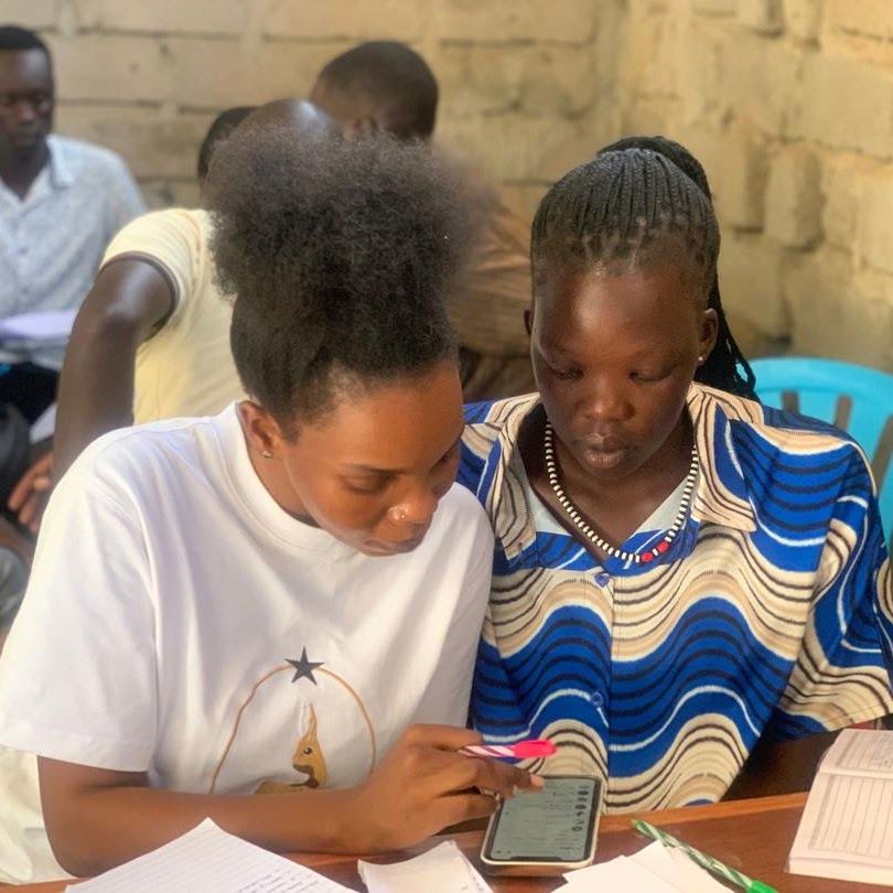 Two young women review work together on a phone and in a notebook